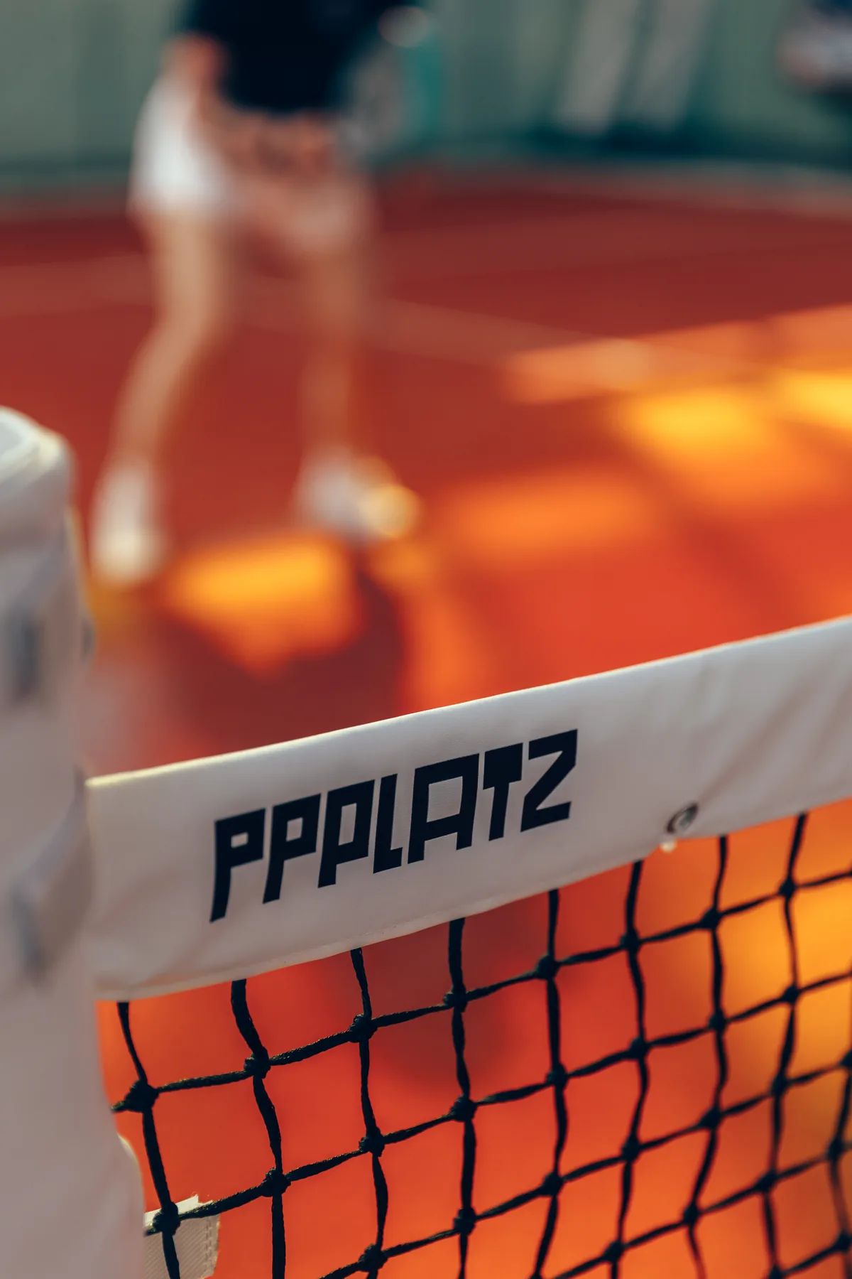 The PPPLATZ wordmark on a padel net in afternoon light